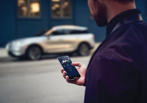 A person is shown interacting with a smartphone to connect to a Lincoln vehicle across the street. | Empire Lincoln of Huntington in Huntington NY