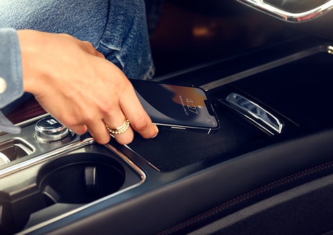 A smartphone is is being placed on the wireless charging pad in the front center console cubby. | Empire Lincoln of Huntington in Huntington NY