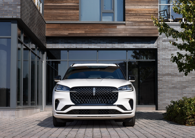 A white 2025 Lincoln Aviator® SUV is shown parked outside a modern building with gray brick and wood accents. | Empire Lincoln of Huntington in Huntington NY