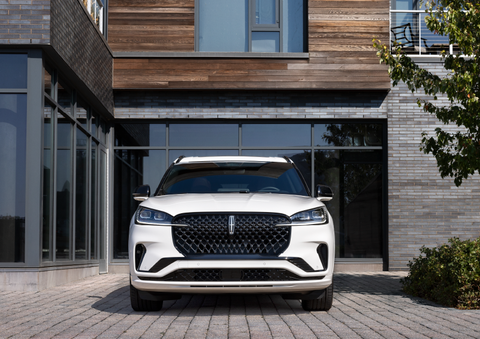 A white 2025 Lincoln Aviator® SUV is shown parked outside a modern building with gray brick and wood accents. | Empire Lincoln of Huntington in Huntington NY