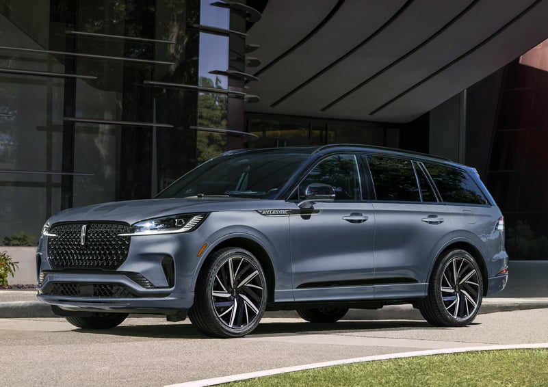 A gray 2025 Lincoln Aviator® SUV is parked outside a modern building showcasing the driver’s side of the vehicle. | Empire Lincoln of Huntington in Huntington NY
