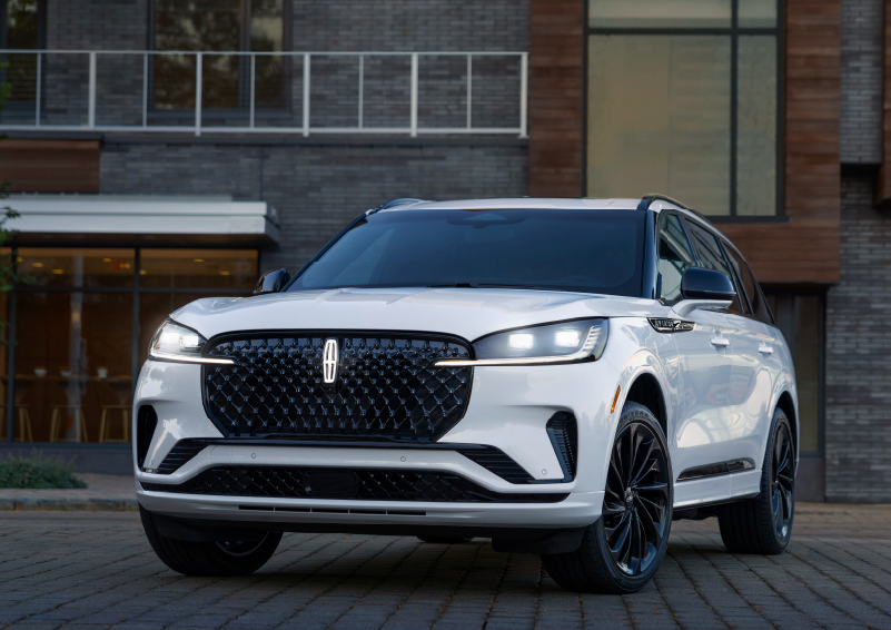 A white 2025 Lincoln Aviator® SUV is shown parked outside a modern building with gray brick and wood accents. | Empire Lincoln of Huntington in Huntington NY