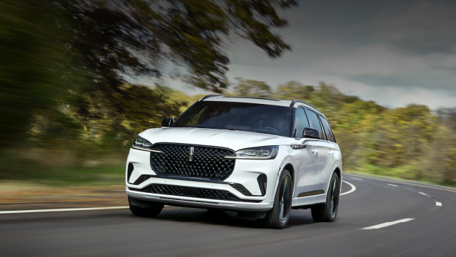 A white 2025 Lincoln Aviator® SUV is being driven down a road lined with trees. | Empire Lincoln of Huntington in Huntington NY