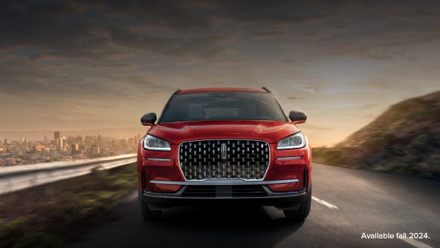 A 2025 red Lincoln Corsair® SUV is being driven down a road at sunset. | Empire Lincoln of Huntington in Huntington NY