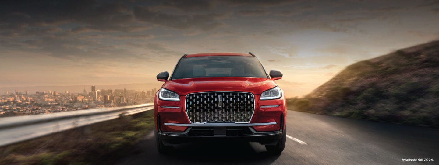A 2025 red Lincoln Corsair® SUV is being driven down a road at sunset. | Empire Lincoln of Huntington in Huntington NY