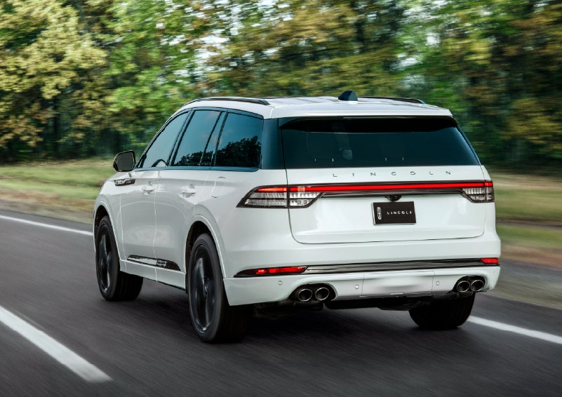 A white 2026 Lincoln Aviator® SUV is being driven away down a road lined with colorful trees. | Empire Lincoln of Huntington in Huntington NY