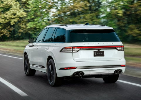 A white 2026 Lincoln Aviator® SUV is being driven away down a road lined with colorful trees. | Empire Lincoln of Huntington in Huntington NY