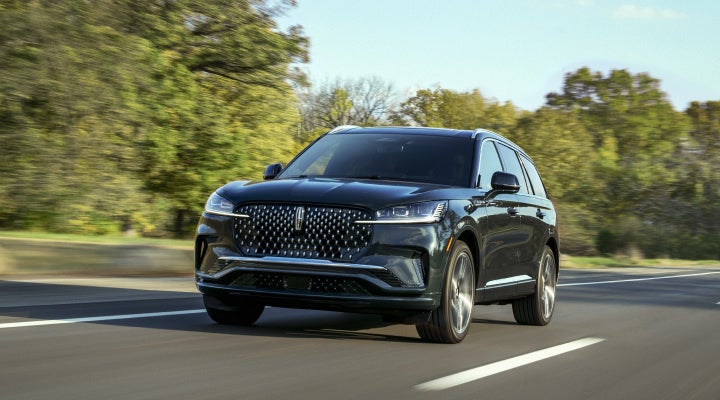 A 2026 Lincoln Black Label™ Aviator® SUV is being driven down a road lined with trees. | Empire Lincoln of Huntington in Huntington NY