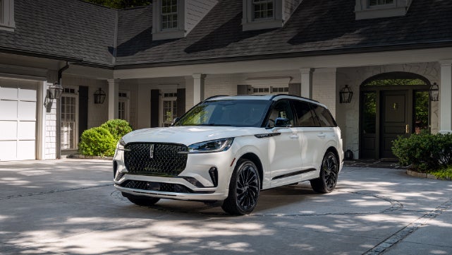 A white 2026 Lincoln Aviator® SUV is parked in the driveway of a luxury home. | Empire Lincoln of Huntington in Huntington NY