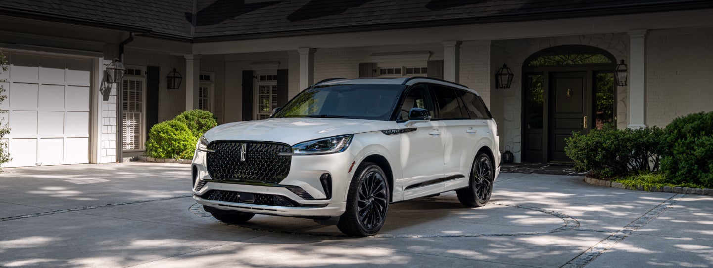 A white 2026 Lincoln Aviator® SUV is parked in the driveway of a luxury home. | Empire Lincoln of Huntington in Huntington NY