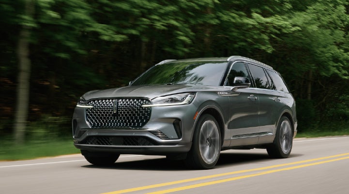 A 2027 Lincoln Aviator® SUV is being driven down a road lined with trees. | Empire Lincoln of Huntington in Huntington NY